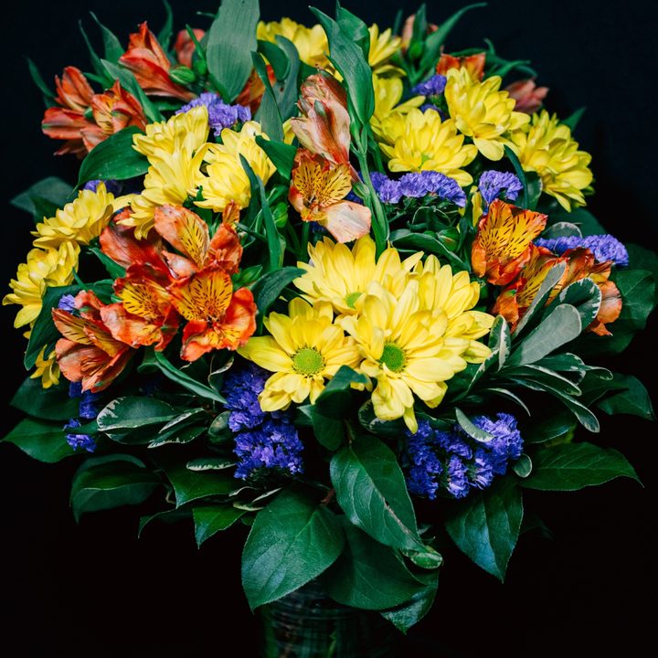 A bright mixed rose and daisy bouquet against a dark background